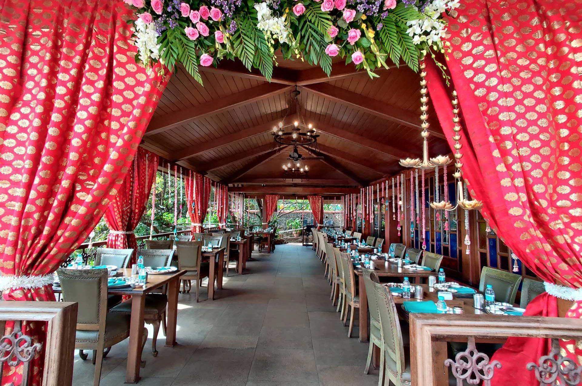 Ramsukh Resort’s outdoor restaurant beautifully decorated with red curtains and floral arrangements.